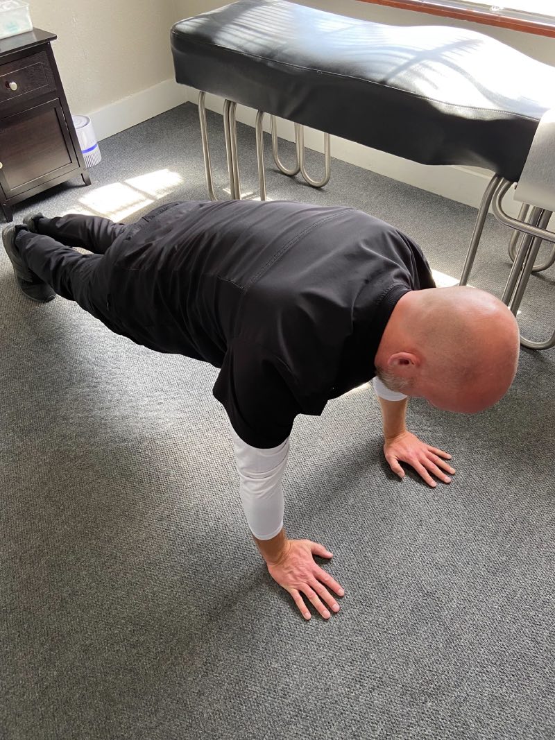 Dr. Daniel Murray: A man in a plank position with his hands and feet flat on the ground.