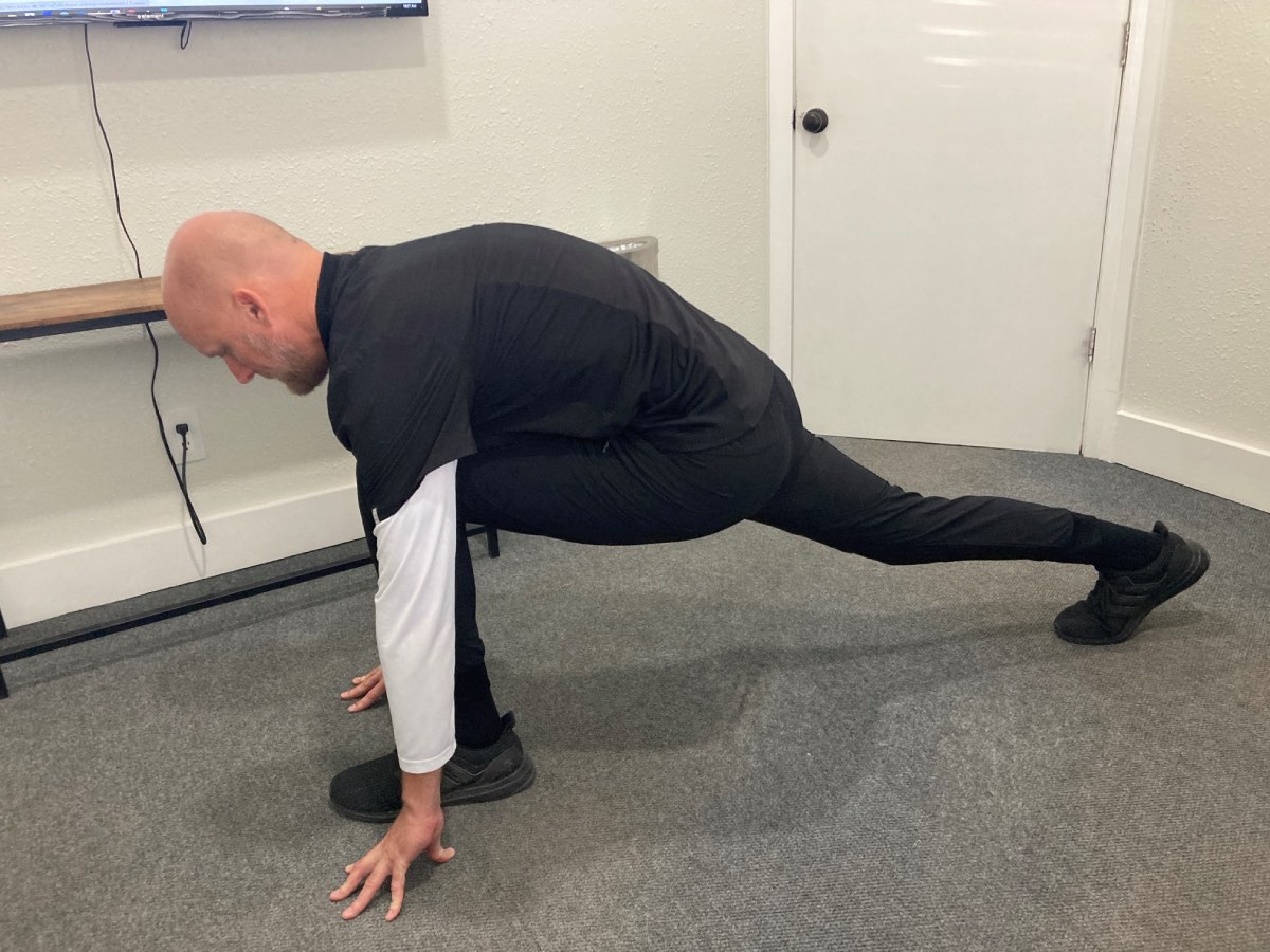 Image of Dr. Daniel Murray: A man is standing up straight, with his hands in a lunge position with his back flat and leg straight back.